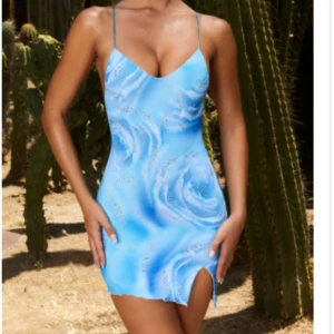 Blå kortklänning med smala axelband - Trendig blå kortklänning med smala axelband och ett abstrakt mönster. Klänningen har en slits framtill och en figurnära passform som framhäver silhuetten. Helt ny ifrån oh polly , aldrig använd. Perfekt för sommaren/ resa 