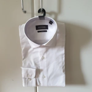 Ny Vit herr skjorta stl S, från Dressmann - Säljer en ny/oanvänd stilren vit skjorta från Dressmann i storlek S. Skjortan är slim fit och gjord av premium bomull med stretch för extra komfort. Den har klassiska knappar framtill och en snygg krage. Perfekt för både formella och avslappnade tillfällen! köpt för 599kr. har befunnit sig i samma hem som en katt 