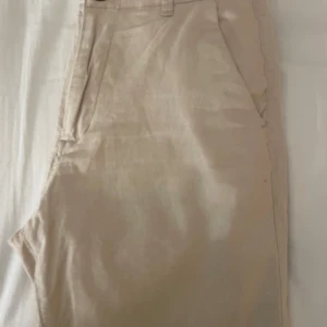 Beige linne shorts från Jack&Jones - Snygga beige chinos från Jack & Jones med klassisk design. Byxorna har en midwaist passform och är tillverkade i ett bekvämt bomullsmaterial. De har både fram- och bakfickor samt en knapp och dragkedja framtill.