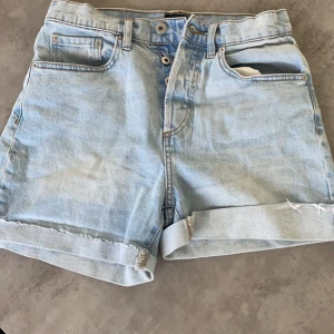 Ljusblå jeansshorts - Snygga ljusblå jeansshorts med upprullade kanter och klassisk femficksdesign. Perfekta för en avslappnad sommarlook. De har en knapp och dragkedja framtill.