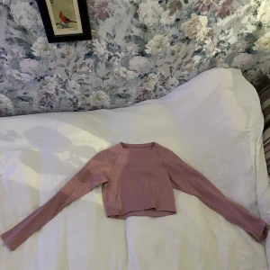 Rosa ribbad croppad tröja - Säljer en söt rosa ribbad tröja med lång ärm och croppad passform. Perfekt för en trendig look. Tröjan har en enkel design med en liten logga på baksidan.