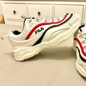 Vita sneakers från Fila - Snygga vita Fila sneakers med röda och svarta detaljer. Skorna har en chunky sula och snörning. Använda, mycket bra skick! 