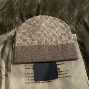 Grå och vit rutig mössa - Snygg grå och vit rutig mössa med uppvikt kant. Perfekt för kyliga dagar och ger en stilren look. Dm för bilder 