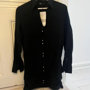 Svart klänning från Zara - Elegant svart klänning från Zara med knappar framtill. Lågmidjad.  Klänningen har långa ärmar och en klassisk krage, perfekt för nyår. Aldrig använd. 