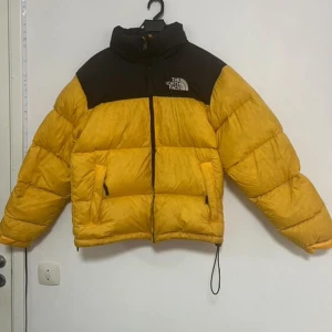 Gul och svart pufferjacka från The North Face - Säljer en snygg gul och svart pufferjacka från The North Face. Jackan har en dragkedja framtill och två praktiska fickor. Perfekt för kyliga dagar med sin varma och vadderade design. Jackan kostar 3500 från butik eller nätet. 