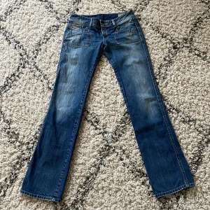 Low waised jeans från Diesel - Snygga blå jeans från Diesel med coola broderade detaljer på bakfickorna. De har en klassisk bootcut-stil och är perfekta för en avslappnad look. Jeansen har en knappgylf och är tillverkade i slitstarkt denim. Pris kan diskuteras 