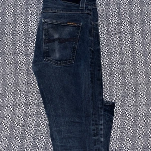 Mörkblå jeans från Nudie Jeans - Snygga mörkblå Grim Tim  jeans från Nudie Jeans med klassisk femficksdesign och subtila slitningar. Perfekta för en avslappnad stil. Märkeslogga på bakfickan ger en extra touch. Den är liten vid midjan och kan vara tajt. 