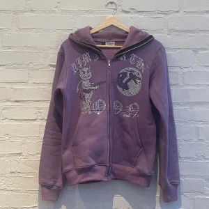 Lila hoodie med strassdetaljer - Säljer en lila hoodie från Aim for the Moon med coola strassdetaljer på framsidan. Tröjan har en dragkedja och en mysig huva. Perfekt för att ge din outfit lite extra bling! 💜