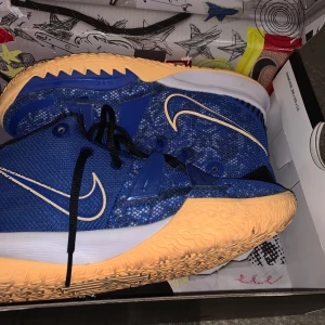 Blå Nike Kyrie 7 sneakers - Säljer ett par blå Nike Kyrie 7 sneakers med orange sula och svarta snören. Skorna har en snygg design med Nike-loggan i kontrasterande färg. Perfekta för basket eller vardagsbruk.