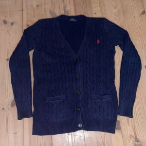 Ralph lauren cardigan - Kabelstickad Ralph lauren cardigan som är mörkblå. Storlek M. Passar som S. Skick 8/10. Kan gå ner i pris vid snabb affär!