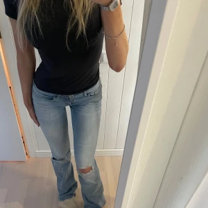 Ljusblå jeans med slitningar - Snygga ljusblå jeans med slitningar på knäna. De har en bootcut-stil och är lågmidjade, vilket ger en avslappnad look. Perfekta för en trendig vardagsstil. Midjemått 80 cm, nypris 699kr, säljer flera jeans på min plick!!!