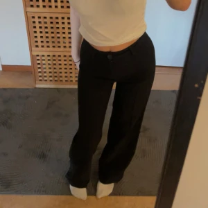 Svarta byxor - Snygga svarta byxor med hög midja och bootcut-stil. Perfekta för en stilren look. Byxorna har en knappdetalj framtill och är tillverkade i ett bekvämt material.