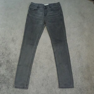 Grå jeans från Bruun & Stengade - Snygga grå jeans från Bruun & Stengade med en slim passform. De har en klassisk design med fem fickor och knappgylf. Perfekta för en stilren look.