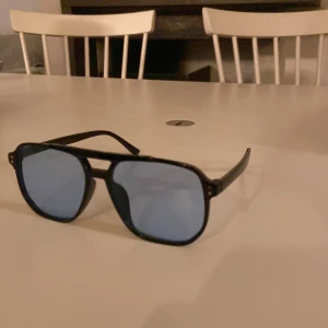 Svarta solglasögon med blå linser - Snygga svarta solglasögon med blå tonade linser. De har en klassisk design med dubbel brygga och fyrkantiga bågar. Perfekta för en stilren look.