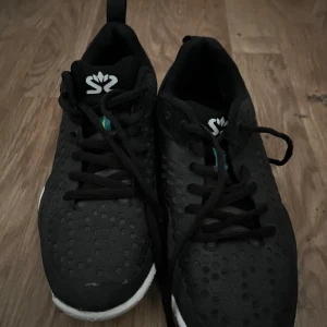 Svarta sneakers från Salming - Snygga svarta sneakers från Salming med vit sula och snörning. Perfekta för träning eller vardagsbruk. Märket 'no nonsense' syns på baksidan av skorna.