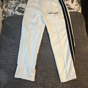 Vita träningsbyxor från Palm Angels - Snygga vita träningsbyxor från Palm Angels med svarta ränder längs sidorna. Byxorna har en elastisk midja och en avslappnad passform. Perfekta för en sportig look. Har använts en gång . Pris går att diskuteras 