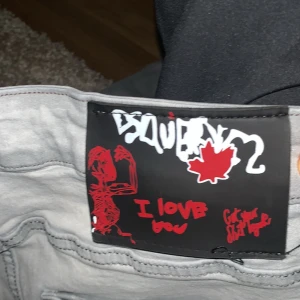 Grå och blå jeans från Dsquared2 - Säljer två par jeans från Dsquared2. Ett par i ljusgrått med slitningar och ett par i mörkblått med distressed detaljer. Båda har en cool och edgy look med unika mönster och detaljer.