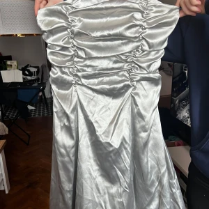 Silverfärgad klänning från Christine - Snygg silverfärgad klänning från Christine med en glansig finish. Klänningen har en åtsittande passform med snörning framtill och är axelbandslös. Perfekt för en elegant kväll! ✨