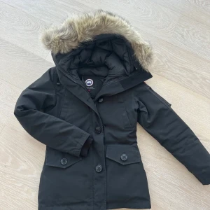 Canada Goose Montebello storlek XS - Svart Canada Goose jacka med pälskrage på huvan, pälsen tas enkelt bort med en dragkedja om man vill. Jackan har knappar framtill och två fickor nedtill, även bra innerficka och en mindre på ena ärmen.  Varm och skön, mycket fint skick, ej sliten. (Jag har köpt jackan på tradera säljer vidare pga storleken inte passade mig)