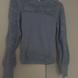 Blå stickad tröja - Säljer en blå stickad tröja med långärmad design och ett fint spetsmönster på ärmar och överdel. Perfekt för kyligare dagar och ger en stilren look. Passar bra till både jeans och kjol.
