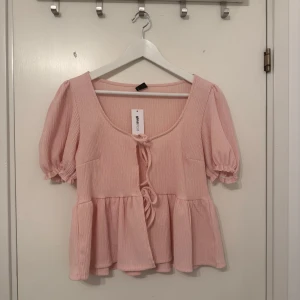 Rosa knytblus från Gina - Säljer en söt rosa blus från Gina i storlek M. Blusen har korta ärmar och knytning framtill. Perfekt för en somrig look! Helt oanvänd och prislappen finns kvar!💕Nypris: 279kr