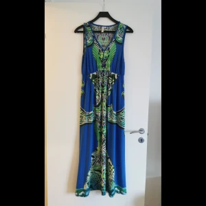 Mönstrad långklänning från Body Flirt - Snygg långklänning från Body Flirt med ett färgglatt mönster i blått, grönt och lila. Klänningen har en v-ringad design och är ärmlös, perfekt för sommarens varma dagar. Den har en avslappnad passform som ger en bekväm känsla.