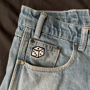 Ljusa jeans från Butter goods - Säljer ett par ljusa jeans från Butter med relaxed loose fit. De har en cool broderad tärning på fickan och en avslappnad stil. Perfekta för en chill look. Dom är rätt så använda och är lite vit färg nere på båda sidorna(1 bilden) 