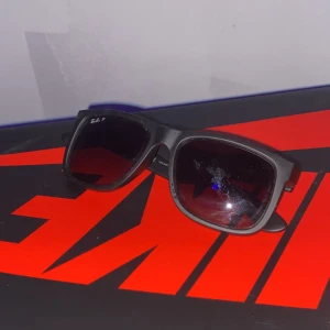 Svarta solglasögon från Ray-Ban - Snygga svarta solglasögon från Ray-Ban med en klassisk design. De har en rektangulär form och mörka linser som ger ett stilrent intryck. Perfekta för soliga dagar och en tidlös accessoar till din outfit.