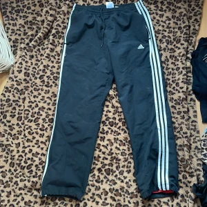 Svarta träningsbyxor från Adidas - Säljer ett par svarta träningsbyxor från Adidas med de klassiska tre vita ränderna längs sidorna. 