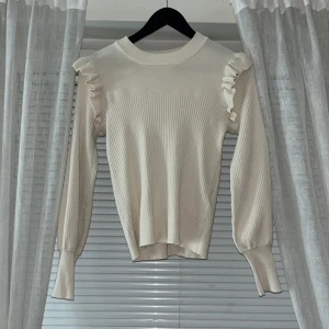 Beige ribbad tröja från Vila - Säljer en stilren beige ribbad tröja från Vila med volangdetaljer på axlarna. Tröjan har långa ärmar och en rund halsringning. Perfekt för en chic och bekväm look. Hör av dig vid intresse! ✨