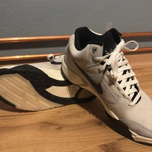 Nike air flight i grått och svart - Snygga Nike sneakers i grått med svarta detaljer och snörning. Skorna har en stilren design med perforerade partier och en robust sula. Perfekta för en sportig look.