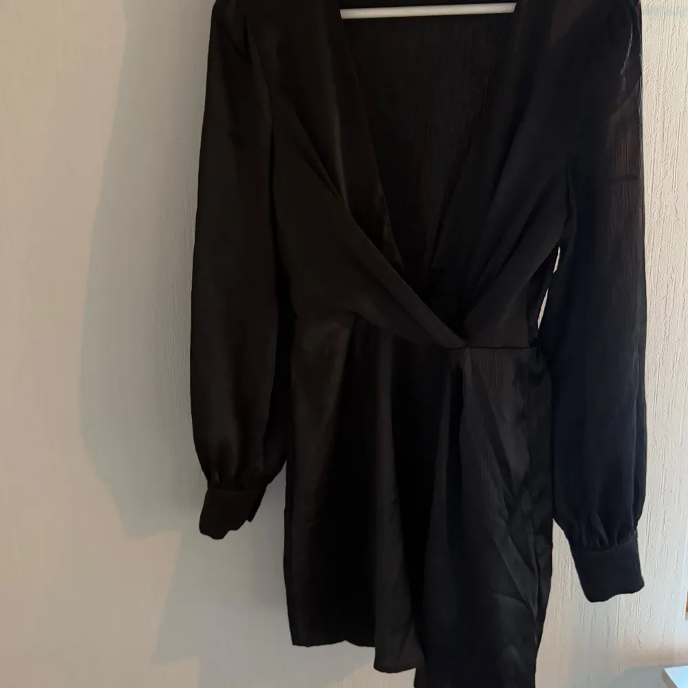 Elegant svart omlottklänning med långa ärmar och v-ringad design. Perfekt för en stilren look.. Mekot.