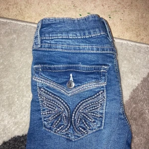 Blå jeans med broderade fickor - Snygga blå jeans med unika broderade detaljer på bakfickorna. De har en klassisk femficksdesign och en bekväm passform. Perfekta för en avslappnad stil. De är juster bara vid midjan. 