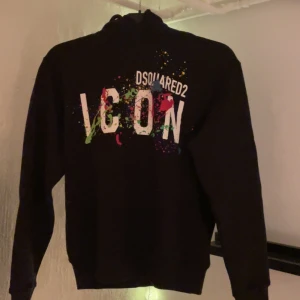 Svart hoodie från Dsquared2 - Snygg svart hoodie från Dsquared2 med färgglada stänk och texten 'ICON' på framsidan. Knappt använd, mycket bra skick! Köpte den i höstas för 4500kr.