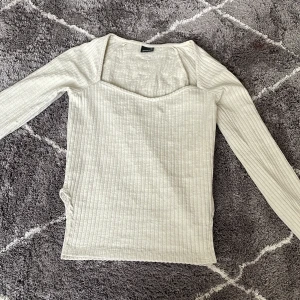 Beige ribbad tröja från Gina Tricot - Snygg beige ribbad tröja från Gina Tricot med långärmad design. Perfekt för en stilren look. Tröjan har en fyrkantig halsringning som ger en modern touch. Passar bra till både jeans och kjol.