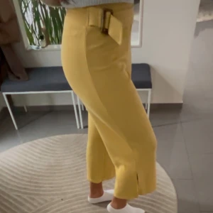 Gula ribbade byxor med bälte - Snygga gula byxor med ribbad textur och ett matchande bälte i midjan. Byxorna har en slits vid bensluten som ger en trendig look. Strechift material 