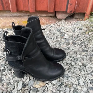 Svarta boots med klack - Snygga svarta boots med klack och spänne. De har en stilren design med en kombination av skinn och mocka. Perfekta för att ge en elegant touch till din outfit.