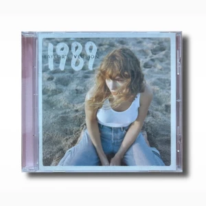 Taylor Swift 1989 (Taylor’s Version) (Rose Garden Pink Edition) Album CD 2023 + poster - Säljer CD:n '1989 (Taylor's Version)' med ett omslag som visar en person på en strand. Inuti finns en rosa CD med fågelmotiv och en bild av en person i vit topp och jeans. Perfekt för fans av popmusik!