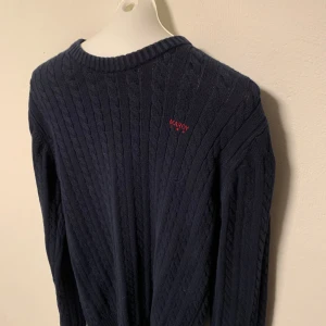 Mörkblå stickad tröja från Maroy - Säljer en snygg mörkblå stickad tröja från Maroy. Tröjan har ett diskret märke på bröstet och ett klassiskt flätmönster. Den är långärmad med ribbstickade muddar vid ärmslut och nederkant. Perfekt för kyligare dagar! Storlek 170/176.