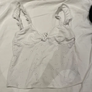 Vit ärmlös topp med broderade detaljer - Säljer en söt vit ärmlös topp med broderade detaljer och rynkade axelband. Perfekt för varma dagar och kan enkelt matchas med olika outfits. Toppen har en fin passform och är både stilren och bekväm.💕 Toppen har en liten grå fläck.