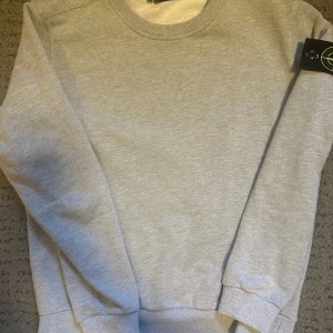 Grå sweatshirt från Stone Island - Säljer en stilren grå sweatshirt från Stone Island. Tröjan har en klassisk rund halsringning och långa ärmar. Perfekt för en avslappnad look. Märkets ikoniska patch finns på ärmen. Passar L och även m. OBS: Fraktas ej! Avhämtning i Göteborgsområdet