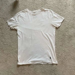 Vit t-shirt från Ralph Lauren - Säljer en klassisk vit t-shirt från Ralph Lauren. Den är kortärmad och har en liten broderad logga i nederkant. Perfekt för en stilren och enkel look.