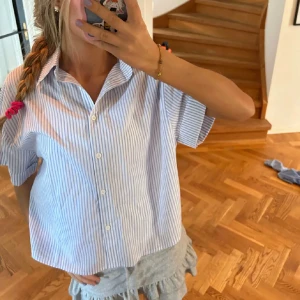 Blå och vit randig skjorta - Säljer en stilren blå och vit randig skjorta med korta ärmar och knappar framtill. Oanvänd 