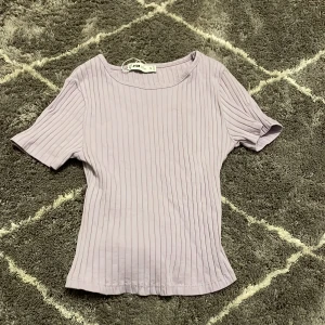 Ljuslila ribbad topp från New Yorker - Säljer en ljuslila ribbad topp från New Yorker i storlek S. Toppen har korta ärmar och en knytning i midjan som ger en snygg detalj. Perfekt för en stilren look! Endast testad.