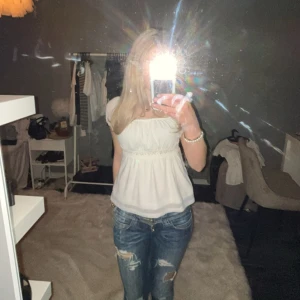 Vit blus med spetsdetaljer - Säljer en söt vit blus med spetsdetaljer vid ärmar och midja. Den har knyt band i ryggen. Blusen har korta ärmar och en luftig passform, perfekt för varmare dagar. Den är gjord i ett lätt och bekvämt material. 💘💘