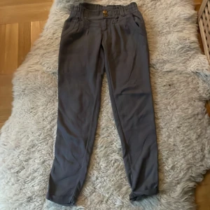 Grå chinos med knappar st.36 - Snygga grå chinos med en klassisk design och knappar i midjan. Perfekta för en stilren look. De har en rak passform och är tillverkade i ett bekvämt material.