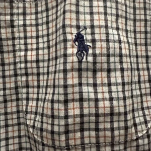 Rutig skjorta från Polo - Säljer en klassisk rutig skjorta från Polo i 100% bomull. Skjortan har en broderad logga på bröstet och knappar framtill. Perfekt för en stilren look.