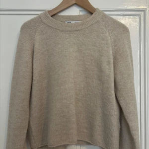 Beige stickad tröja från Zara - Säljer en stilren beige stickad tröja från Zara. Tröjan har en rund halsringning och långa ärmar, perfekt för kyligare dagar. Den är mjuk och bekväm, vilket gör den till ett mångsidigt tillskott i garderoben.