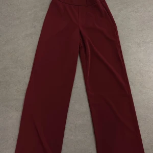 Vinröda byxor från Bik Bok - Snygga vinröda byxor från Bik Bok med hög midja och vida ben. Perfekta för en stilren look. Byxorna har en dragkedja i sidan för enkel påklädning.