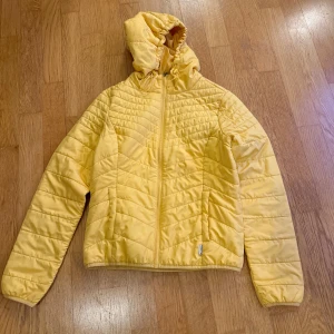 Gul tunn dunjacka från ONLY - Säljer en snygg gul tunn dunjacka från ONLY. Jackan har en dragkedja framtill och en praktisk huva. Perfekt för kyligare dagar med sin varma och bekväma design. Den har en stilren look. Passar perfekt för höst och vår, mellansäsong.